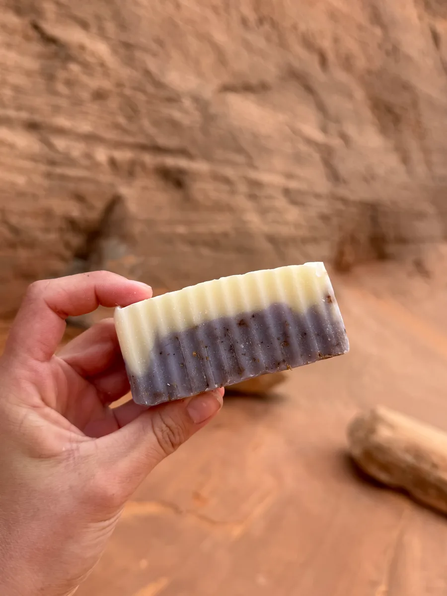 Handmade bar soap, two-tone lavender and cream, held against red sandstone
