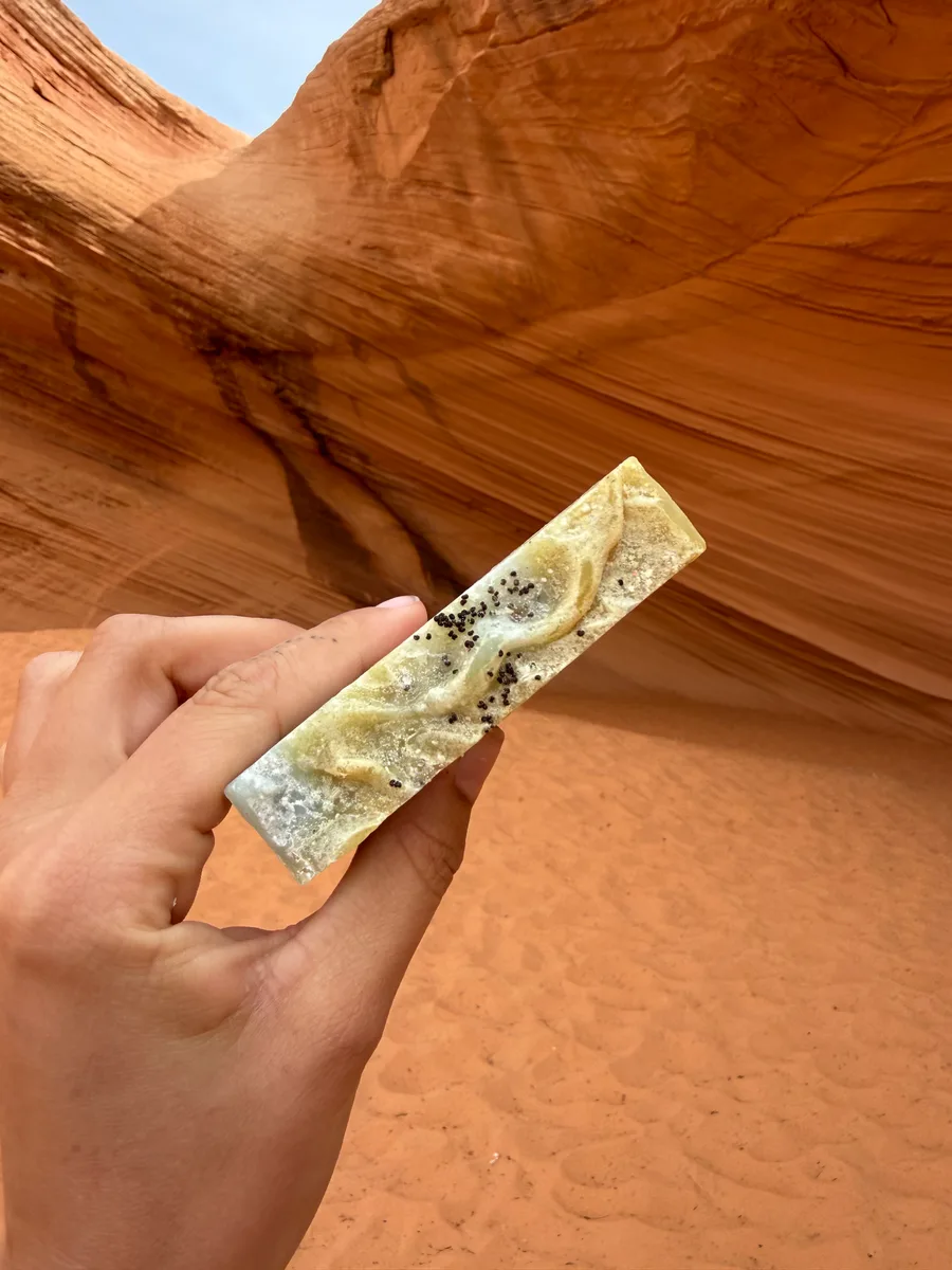 Handmade bar soap, golden with botanicals, held in a slot canyon